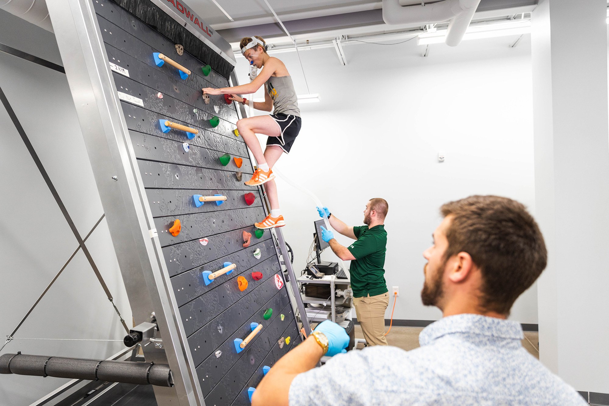 Student climbing on an indoor wall with a breathing apparatus attached